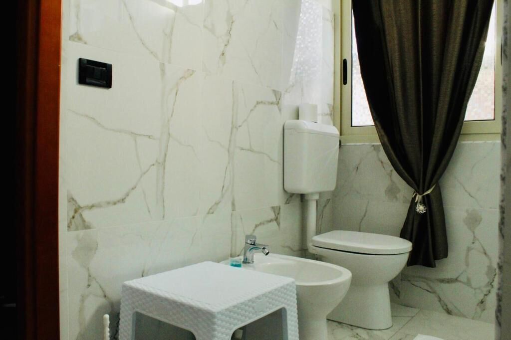 A bathroom with a marble wall, a toilet, a bidet, and a sink with a towel.