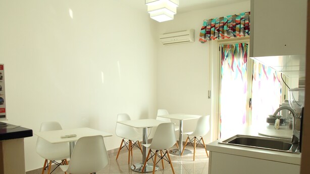A modern kitchen with white appliances, a sink, and a dining area with white chairs and tables. - BEAUTY HOUSE (Reggio Calabria)