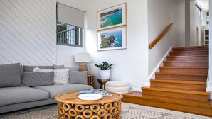 A living room with a grey sofa, a round wooden coffee table, a staircase, and two framed coastal photographs on the wall.