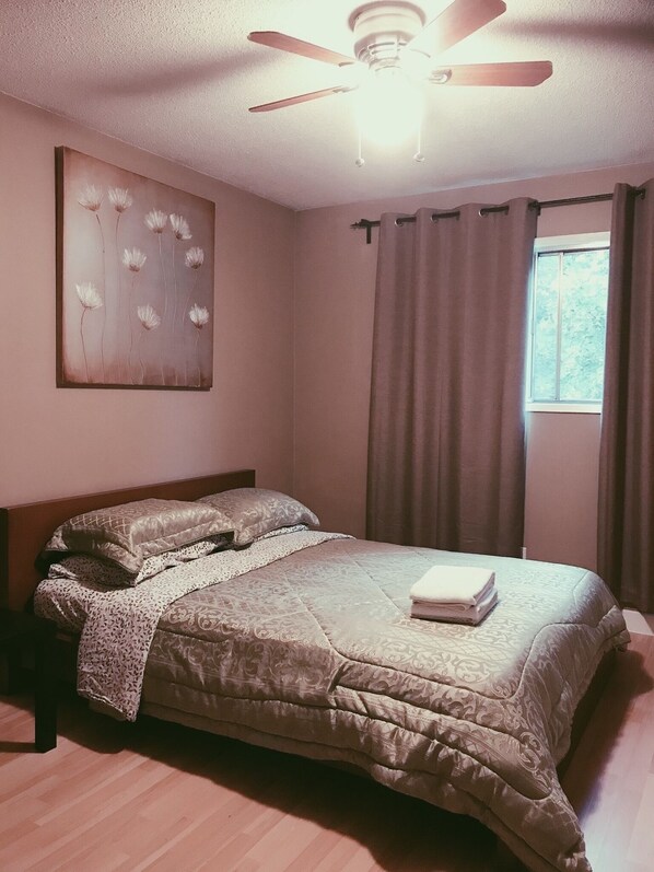 A neatly made bed with a quilt, a ceiling fan, and a window with curtains.