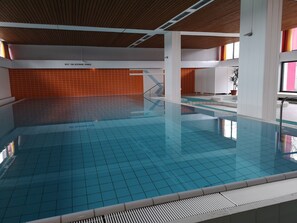 Ein Innenpool mit gefliestem Boden und Wänden, einer Holzbalkendecke und einem sichtbaren Schild auf Deutsch.