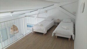 Habitación espaciosa con techos altos, dos camas, un balcón con barandilla blanca y una lámpara colgante.