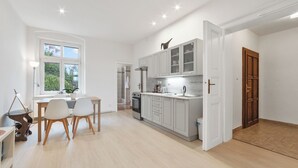 A modern kitchen with white cabinets, a dining area with a table and chairs, and a view of the outdoors through a window.