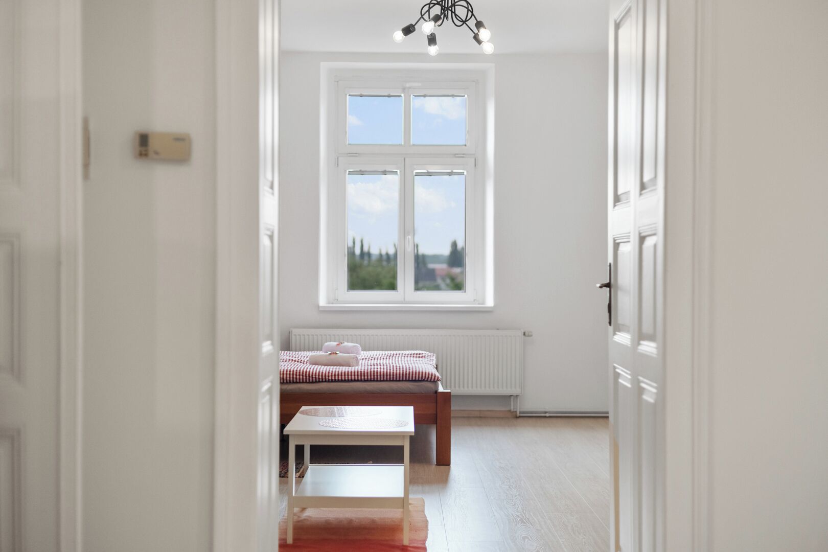 A room with a bed, a table, and a window with a view of trees and buildings.