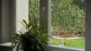 A view through a window of a patio area with a table and chairs, a small statue, and a potted plant.