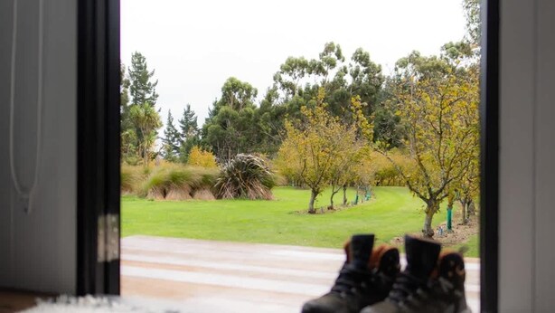 A pair of boots on a rug, a view of a grassy area with trees and shrubs. - Mona Vale Country Estate by Tiny Away (Waikari)