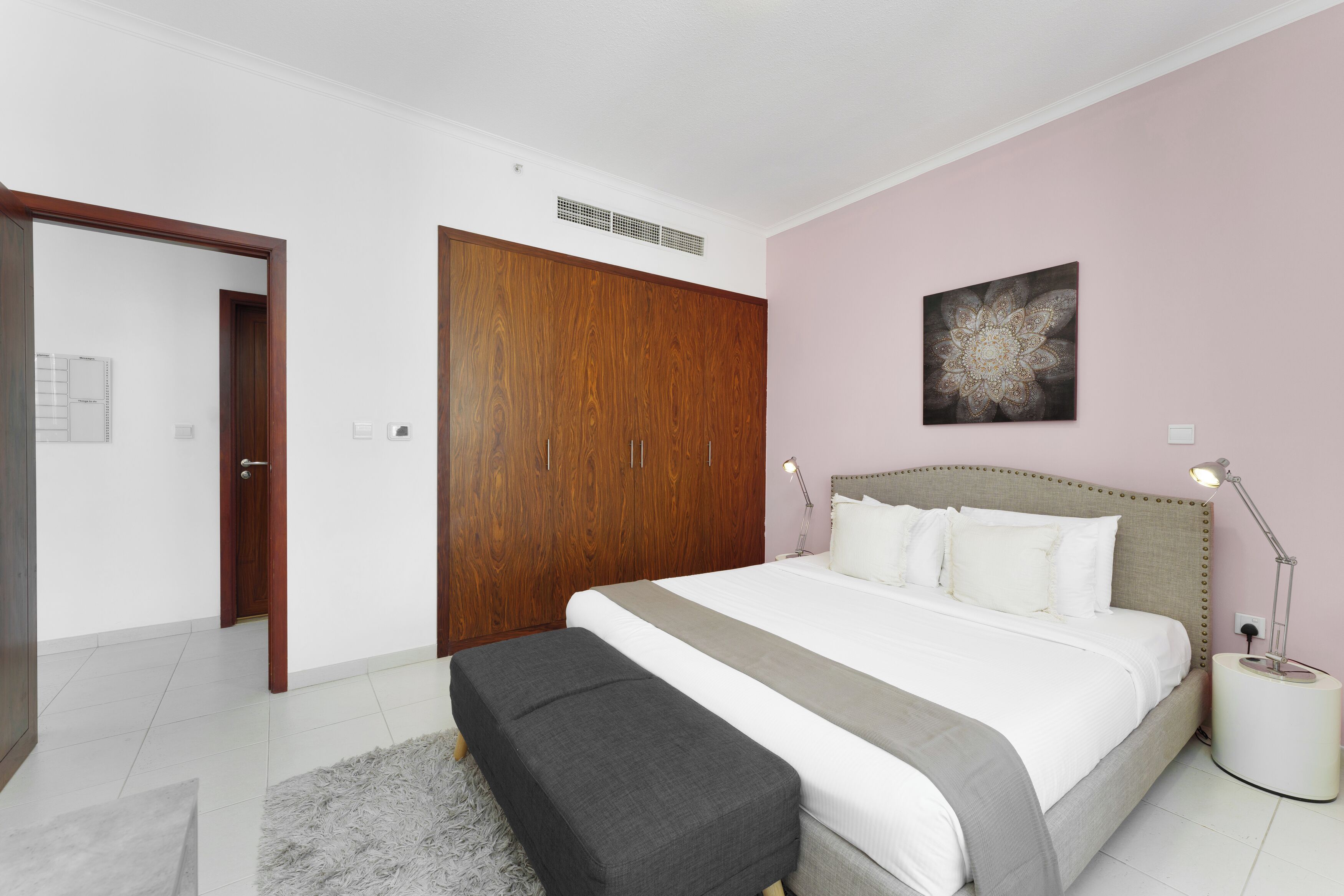 A bedroom with a bed, a wooden wardrobe, a nightstand, and a wall art piece.