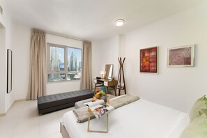 Una habitación de hotel moderna con un ventanal grande, una cama, un sofá, un escritorio y obras de arte en las paredes.