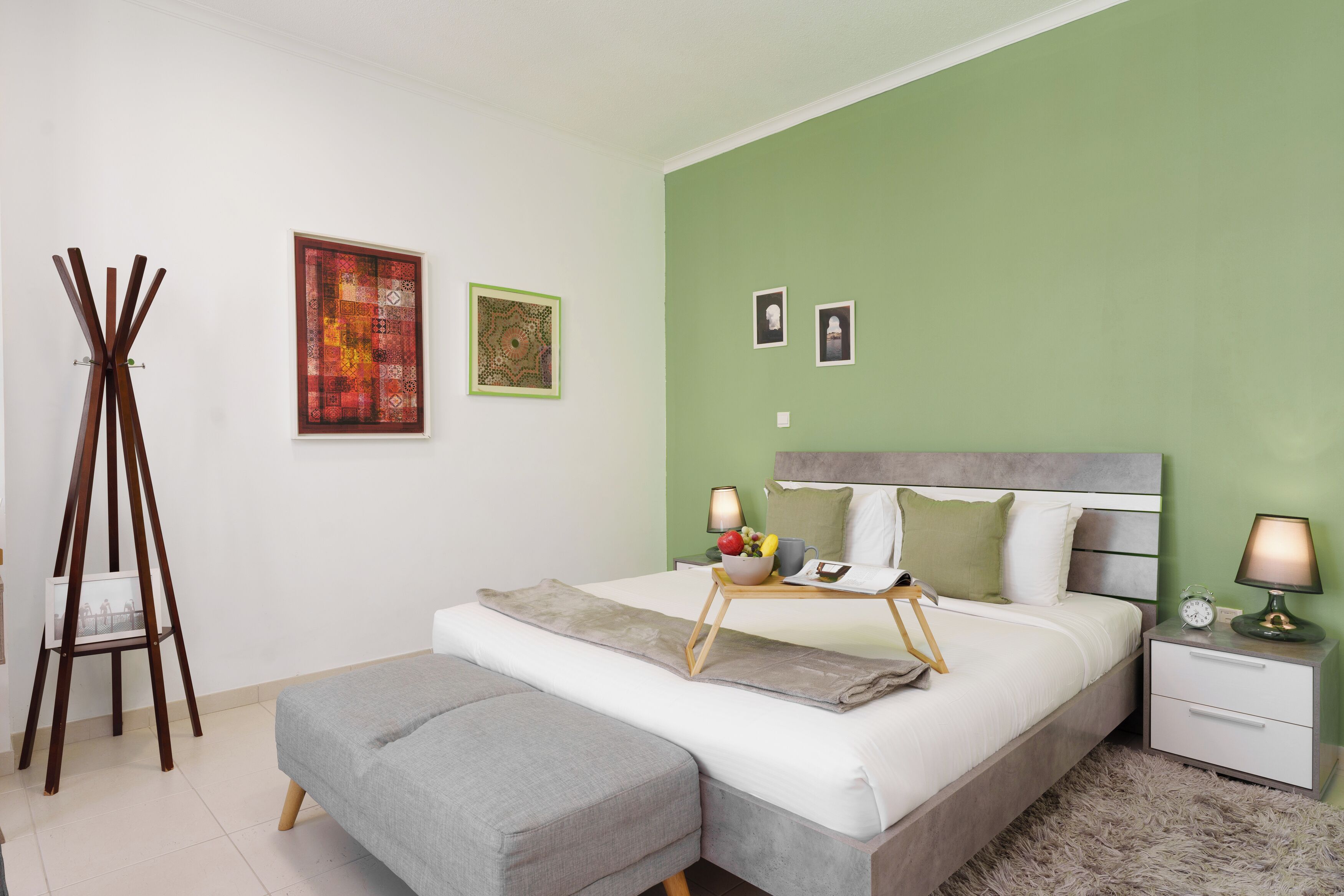 A modern bedroom with a bed, bedside tables, a bench, and artwork on the walls.