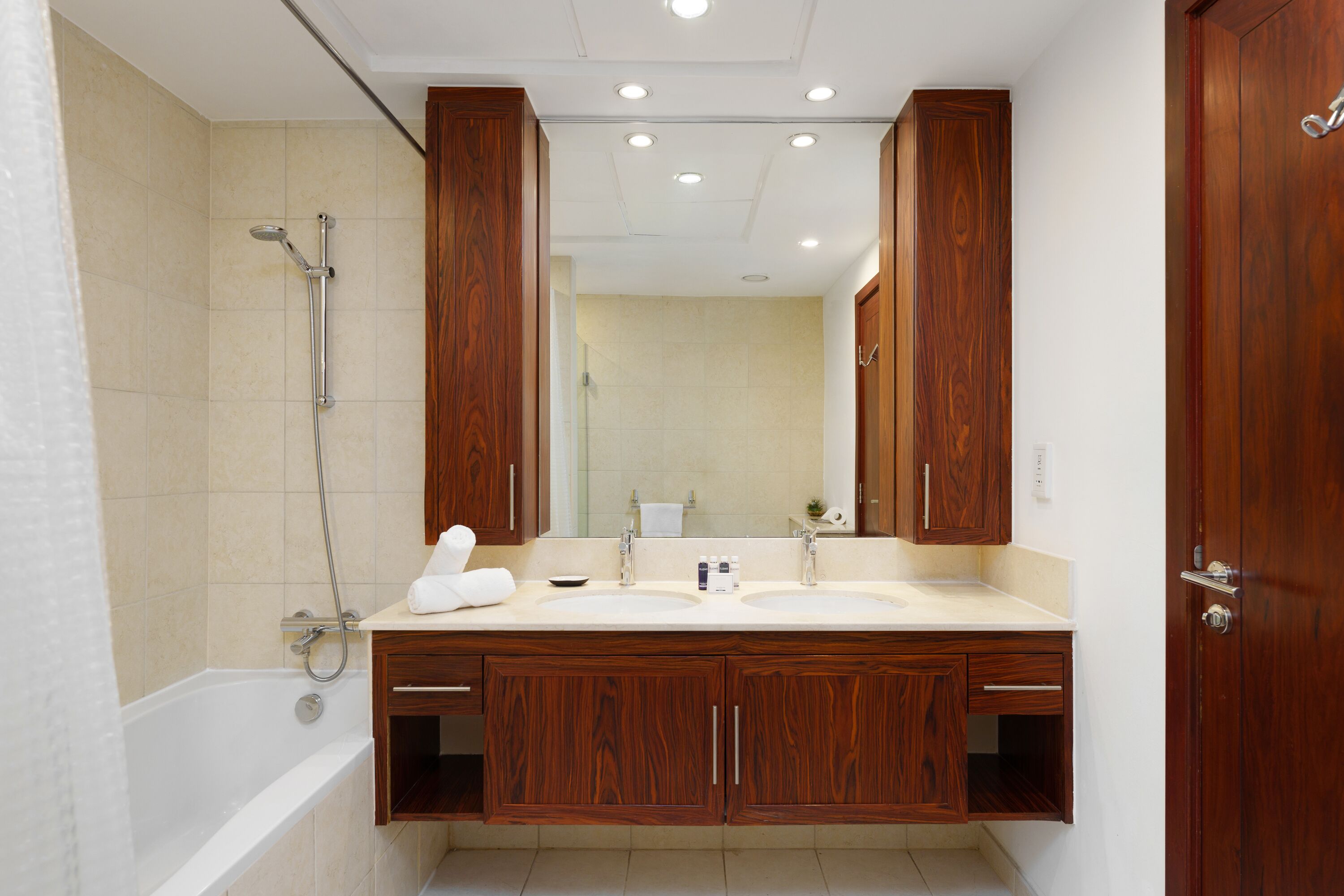 A bathroom with a bathtub, two sinks, wooden cabinets, and a large mirror.
