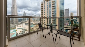 Un balcon avec une table et des chaises, donnant sur un paysage urbain composé de grands immeubles et d’une étendue d’eau.