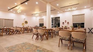 Uma ampla sala de jantar com várias mesas e cadeiras, um tapete estampado e um candelabro.