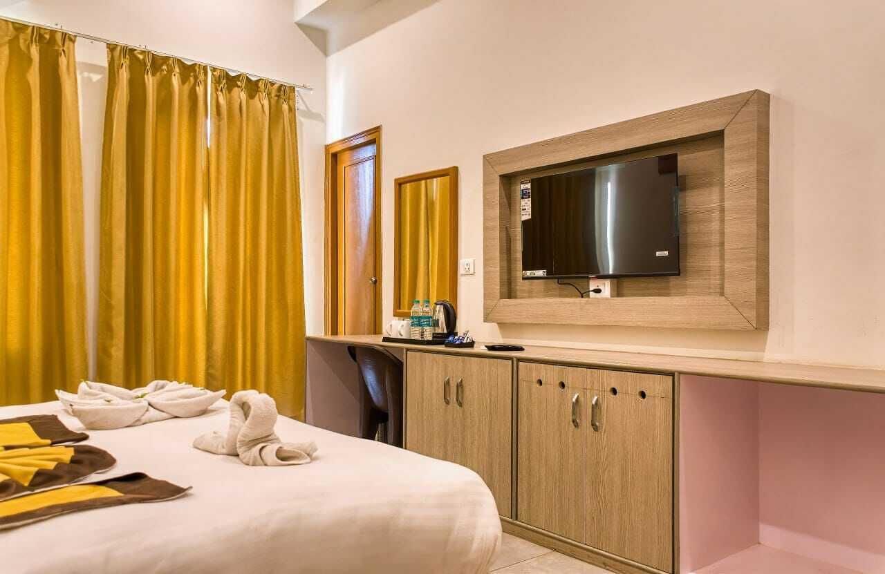 Quarto de hotel com cama, televisão na parede, secretária com cadeira e guarda-roupa.