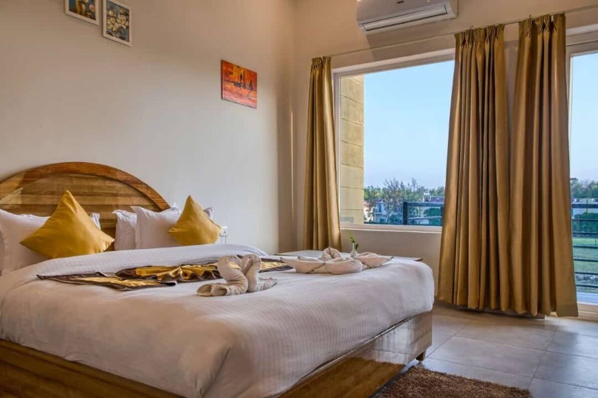 Une chambre d’hôtel avec un grand lit, une tête de lit en bois et une vue sur la ville par une fenêtre ornée de rideaux.