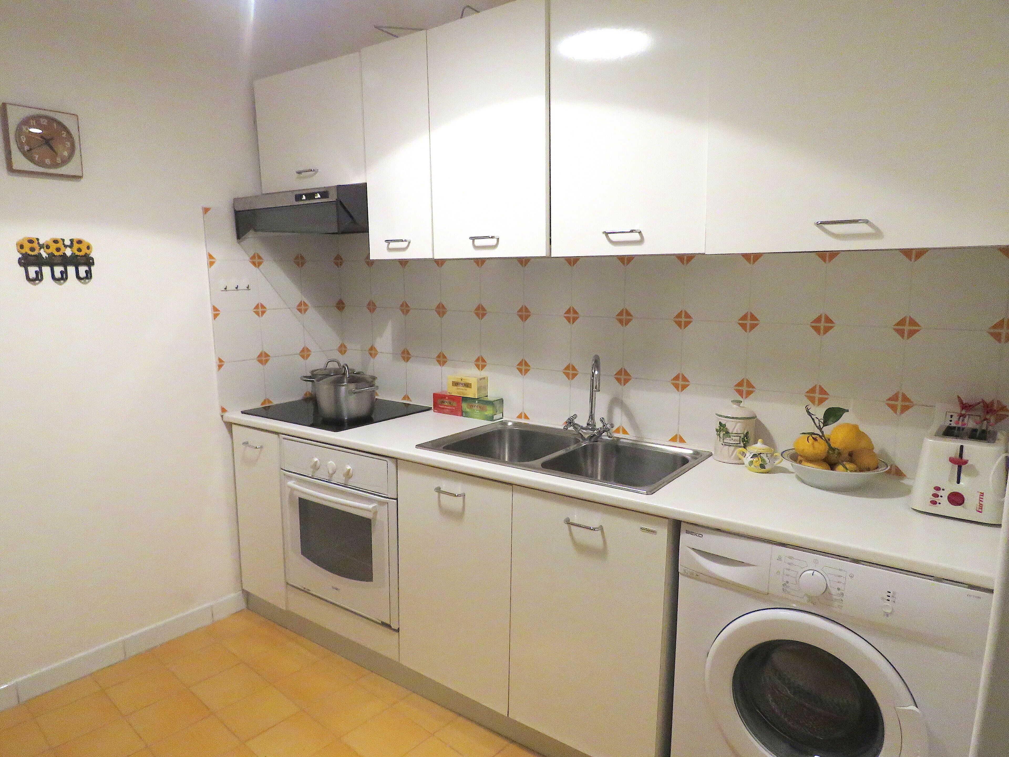 A compact kitchen with white cabinets, a stove, an oven, a sink, and a washing machine.