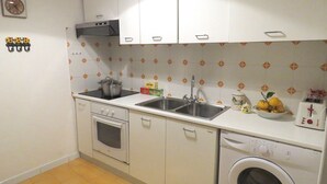 A compact kitchen with white cabinets, a stove, an oven, a sink, and a washing machine.