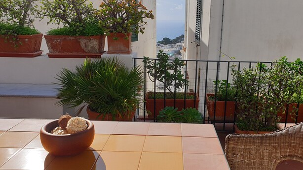 A balcony with terracotta planters, a wicker chair, and a bowl of snacks.