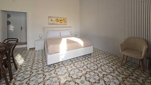 A bedroom with a bed, a chair, a nightstand, a wall with a striped pattern, and a door.