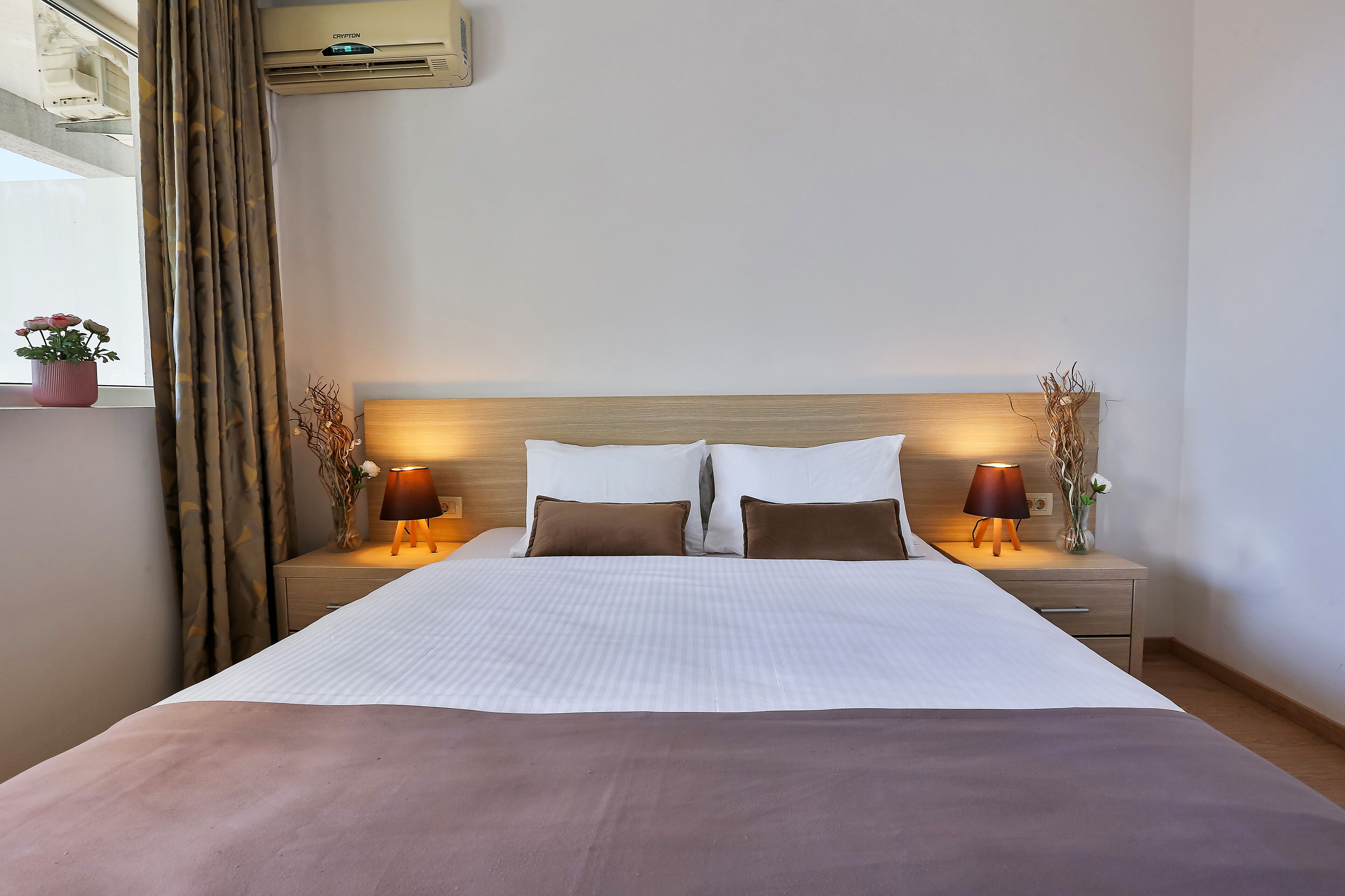A neatly made bed with a wooden headboard, two bedside lamps, and a nightstand with a vase of dried branches.