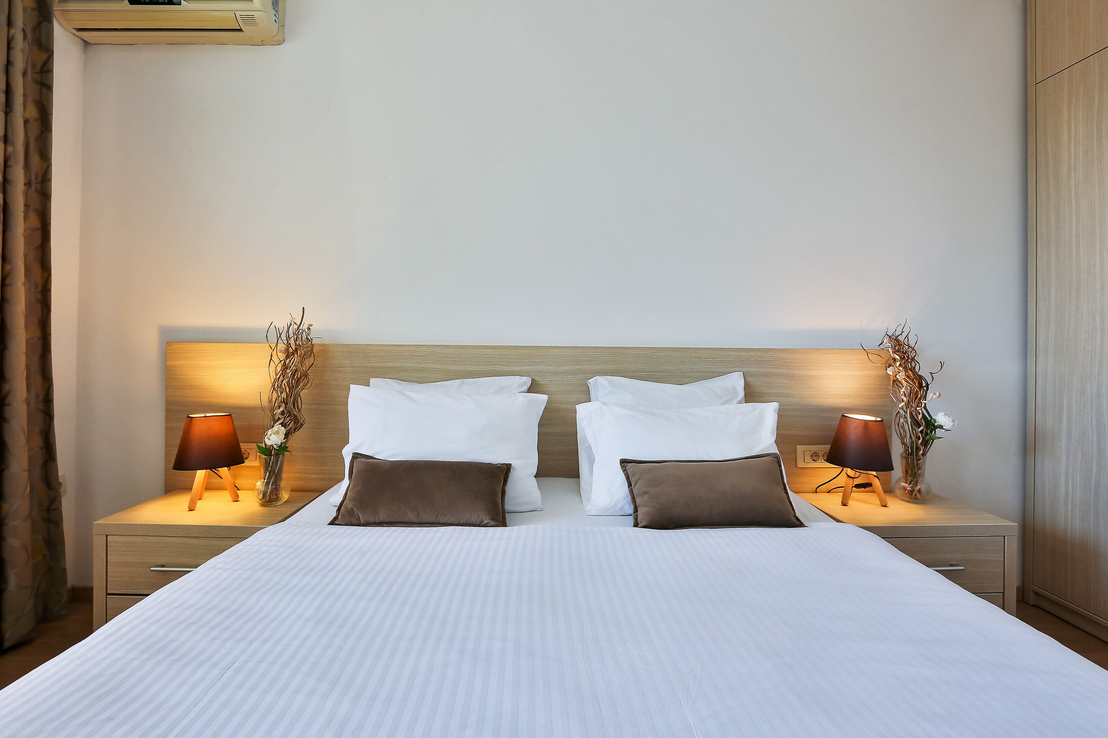 A neatly made bed with white linens, two bedside tables with lamps, and a wooden headboard.