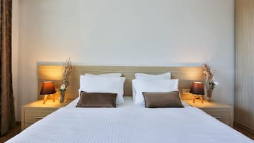 A neatly made bed with white linens, two bedside tables with lamps, and a wooden headboard.