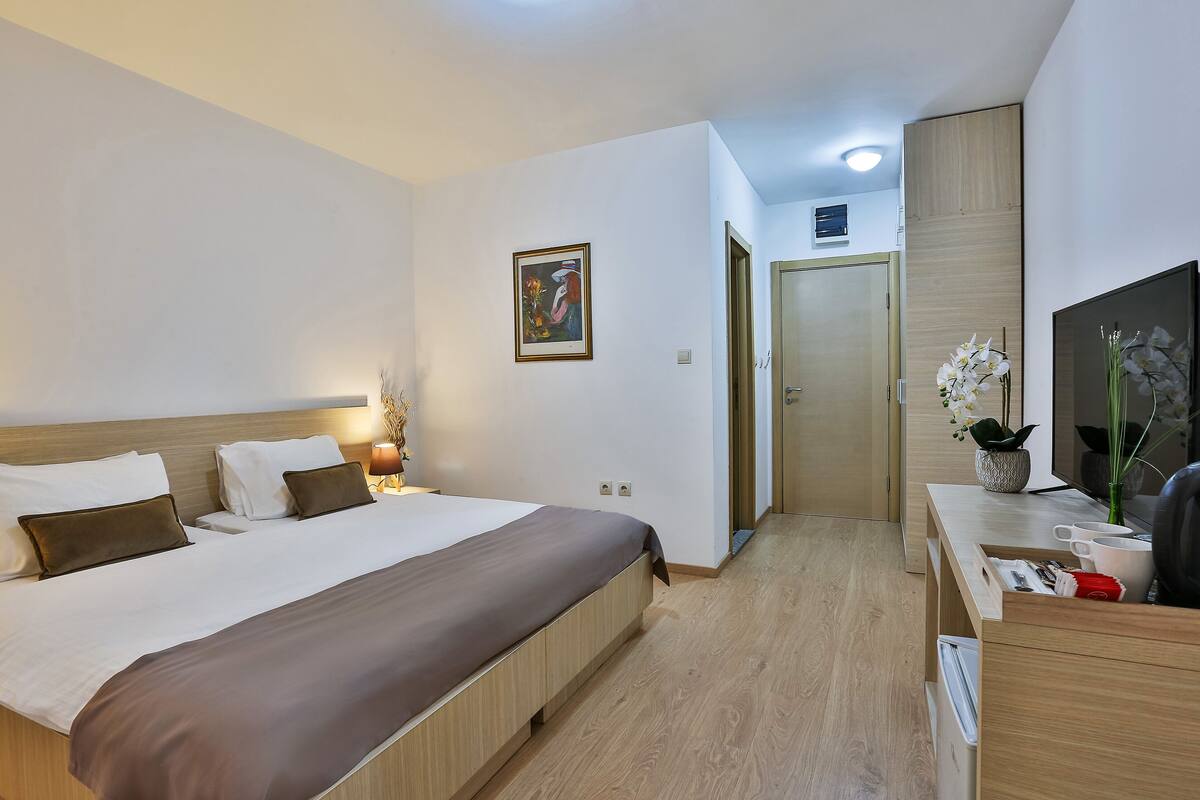 Una habitación de hotel con cama, mesita de noche, lámpara y un cuadro en la pared.