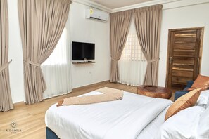 Ein Hotelzimmer mit einem großen Bett, einem an der Wand montierten Fernseher und einer Holztür.