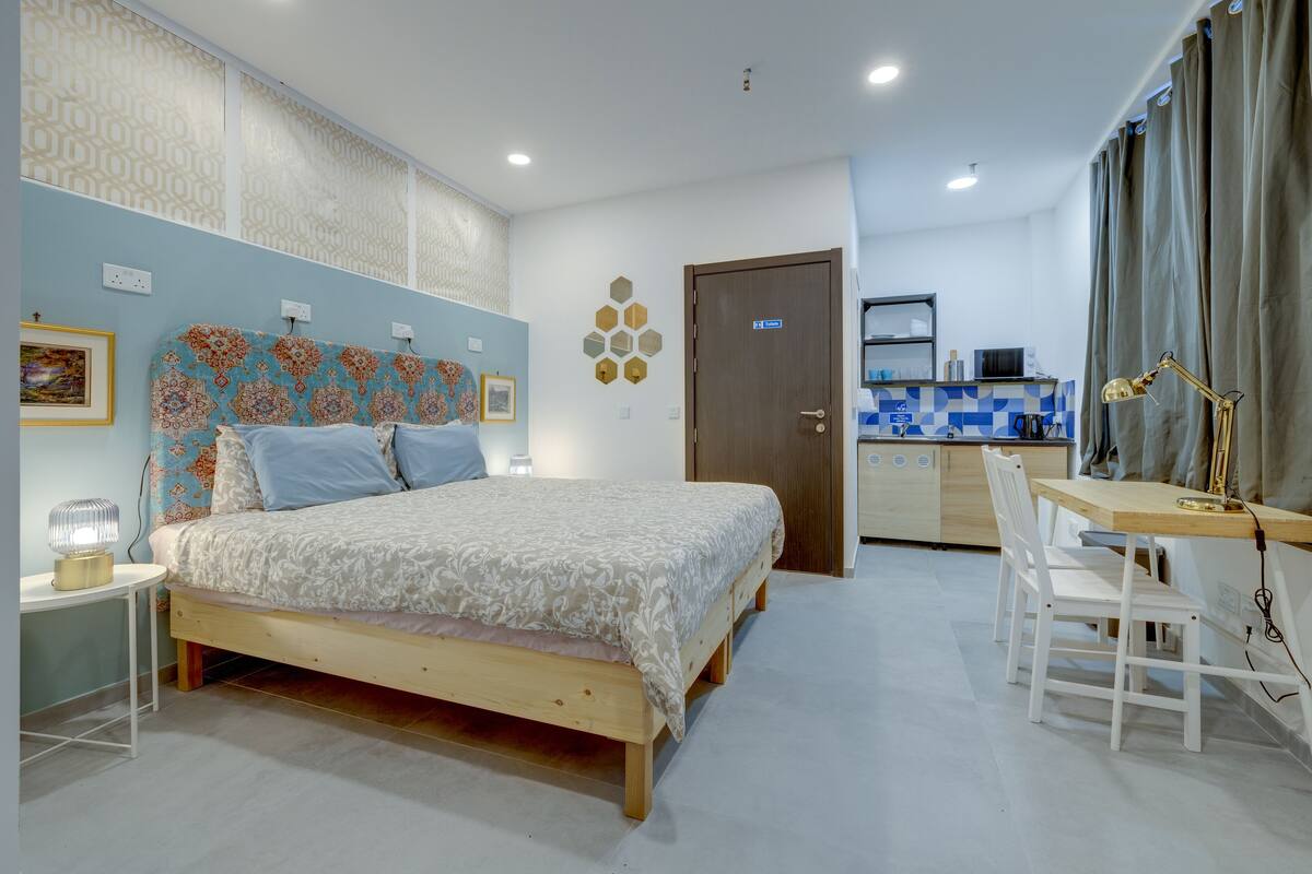 Een slaapkamer met een bed, nachtkastje en een bureau met stoelen.