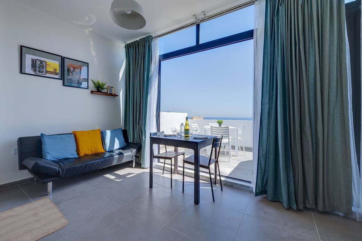 Een moderne woonkamer met een bank, een eettafel en uitzicht op zee.