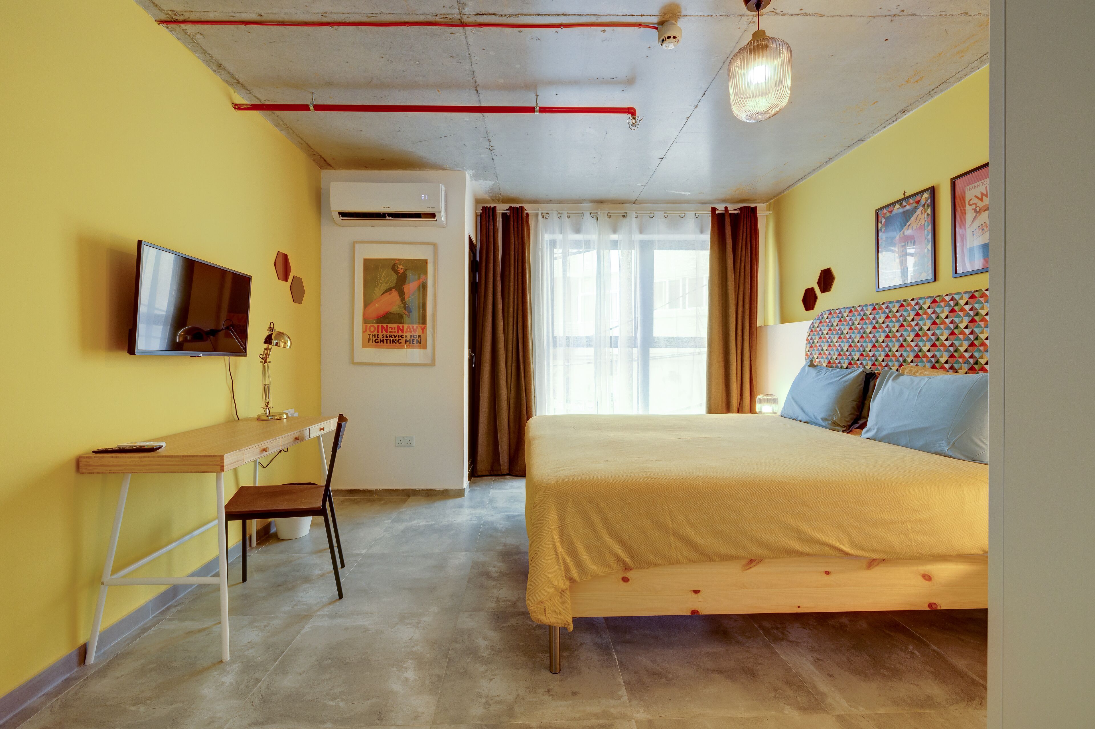 A room with a bed, a desk, a chair, a television, and a window with curtains.