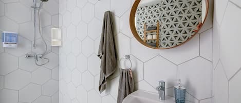 A bathroom with a white sink, a mirror with a geometric pattern, a shower with a hexagonal tile wall, and a towel rack.