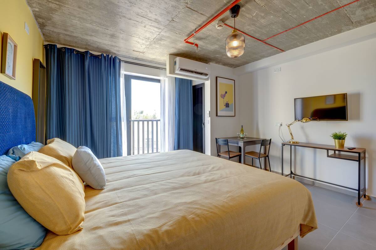 Een hotelkamer met een bed, bureau, stoel, televisie en een balkon.