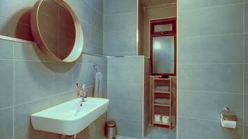 A bathroom with a sink, mirror, toilet paper holder, and a small trash bin.
