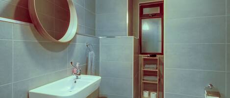 A bathroom with a sink, mirror, toilet paper holder, and a small trash bin.