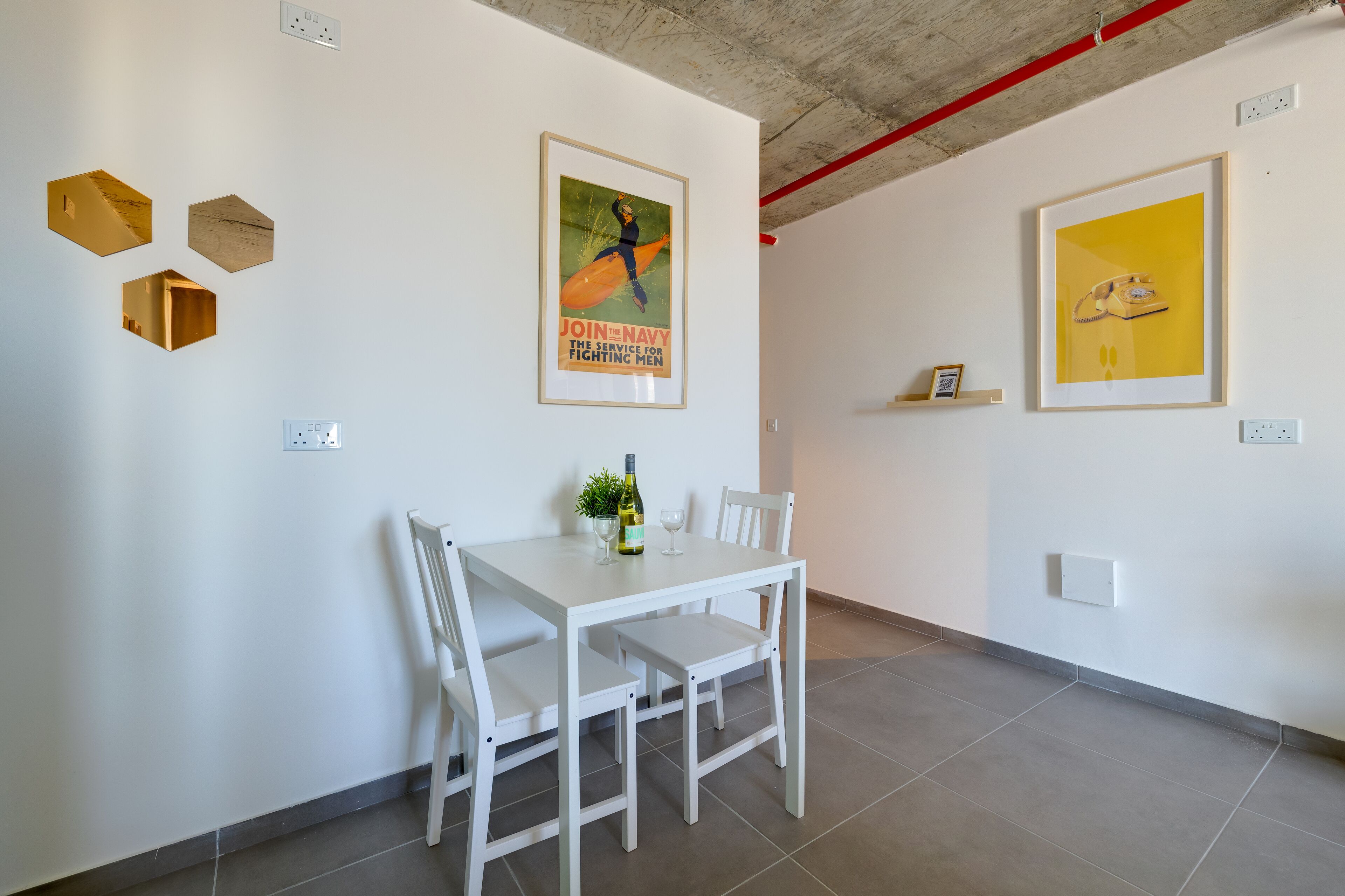Een eetgedeelte met een witte tafel en stoelen, een lijst met een poster en een lijst met een kunstwerk aan de muur.