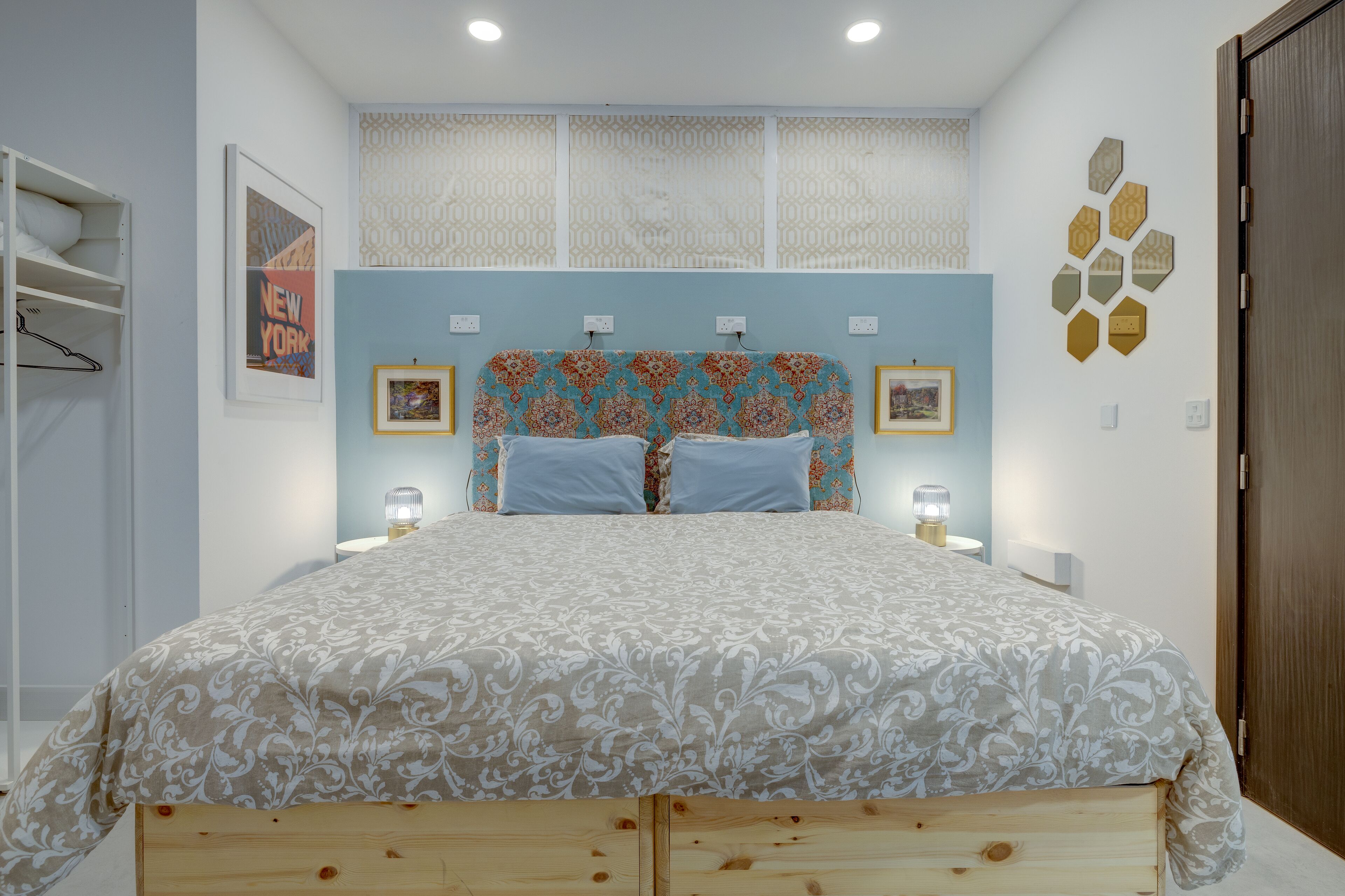 A bedroom with a patterned bedspread, a headboard with a geometric design, and a wall-mounted light fixture.