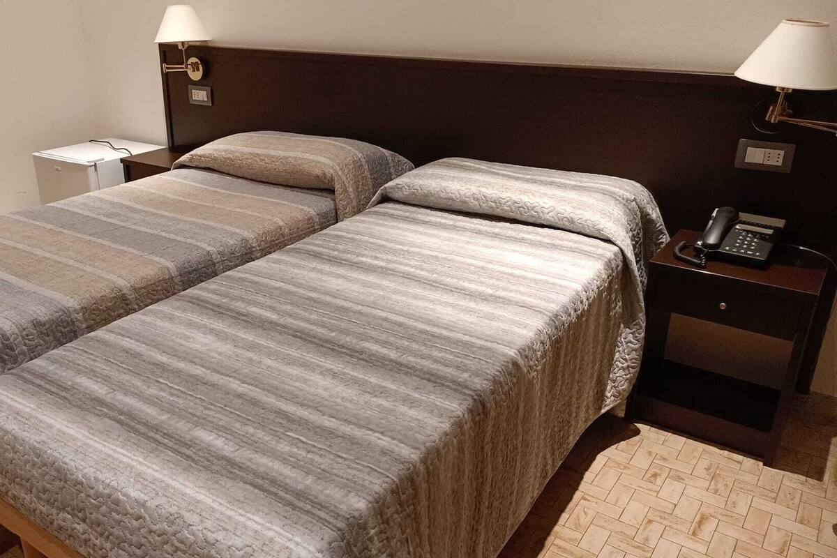 A hotel room with two single beds, a bedside table with a lamp, a phone, and a small desk with a chair.