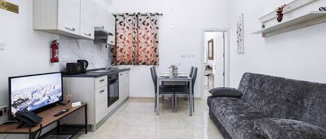 A modern kitchen with a dining area, a sofa, and a TV.