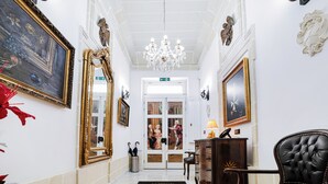 Een statige hal met weelderige decoraties, waaronder een kroonluchter, ingelijste kunstwerken en een grote spiegel.