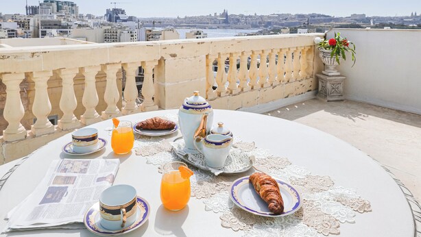 Ontbijt op een balkon met uitzicht op de stad, inclusief een tafel met borden, bekers, een kan sinaasappelsap en een croissant.