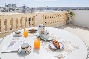 Ontbijt op een balkon met uitzicht op de stad, inclusief een tafel met borden, bekers, een kan sinaasappelsap en een croissant.