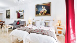 Een hotelkamer met een groot bed, twee nachtkastjes, een bank, een kroonluchter en een schilderij aan de muur.