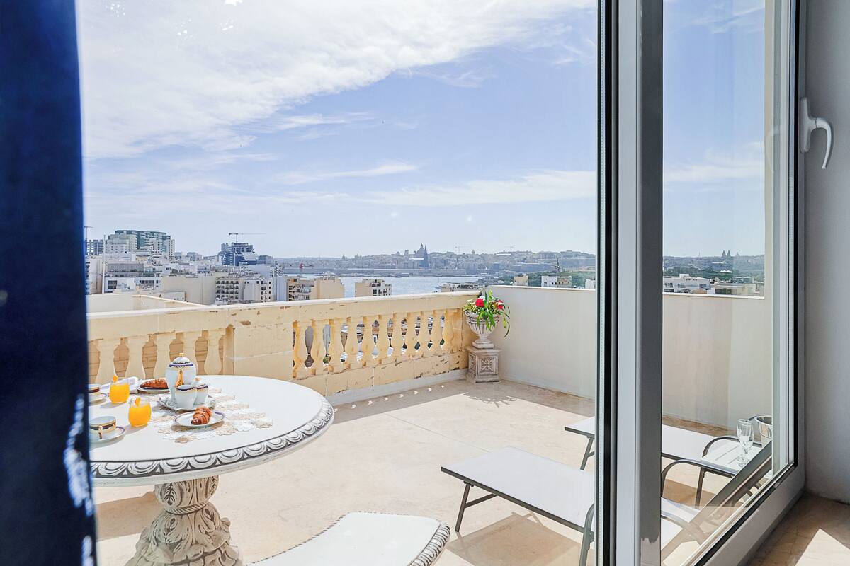 Un balcon avec une table dressée pour le petit-déjeuner, une plante en pot et une vue sur le paysage urbain.