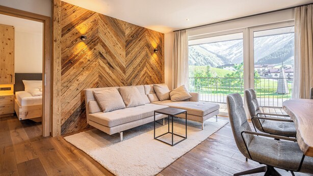 A modern living room with a herringbone wood wall, a sofa, a coffee table, and a dining area with chairs. - TOP 6 - Großzügiges Apartment mit Bergblick (Berwang)
