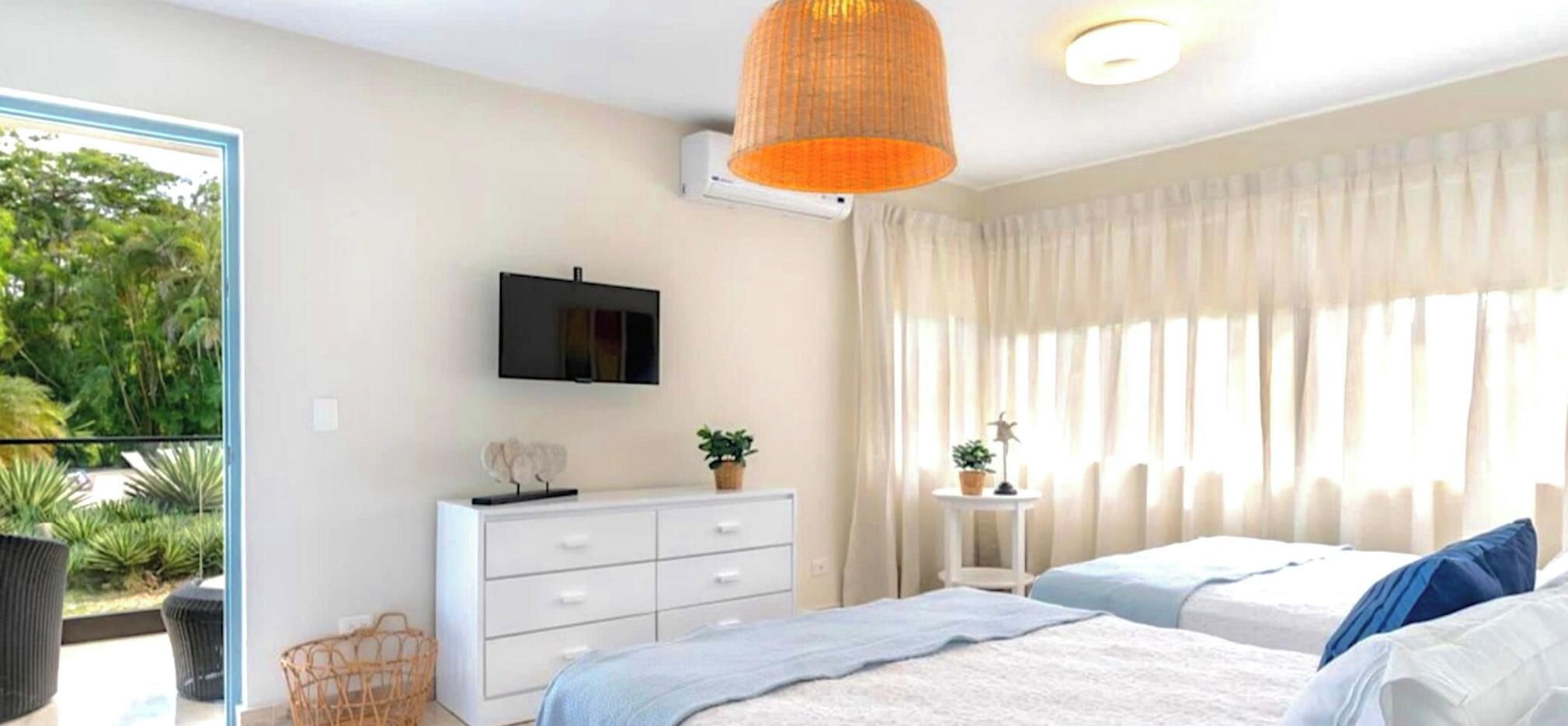 A bedroom with two beds, a TV, a dresser, and a window with curtains.
