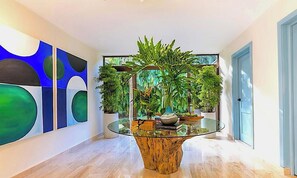 A modern interior with a glass-top table surrounded by potted plants, a large abstract painting on the wall, and a blue door. - Srvittinivillas / Family/ Best Loc/ Casa de Campo Resort / Spacious/confort/golf (La Romana)