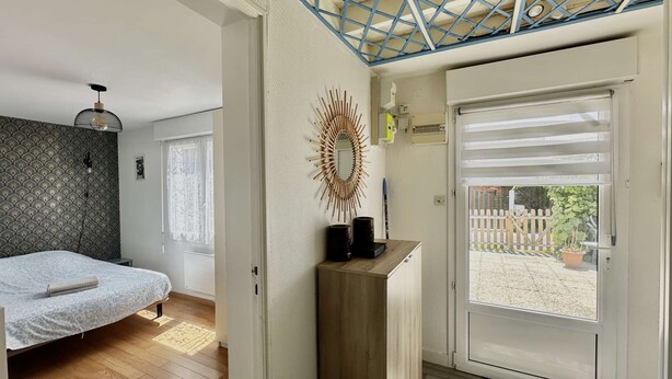 A bedroom with a bed, a wooden dresser, a mirror, and a door leading to a balcony. - Captain's Quarters - Maison en Bord de Plage (Saint-Côme-de-Fresné)
