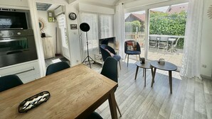 A modern kitchen with built-in appliances, a dining area with a wooden table, and a balcony with outdoor furniture. - Captain's Quarters - Maison en Bord de Plage (Saint-Côme-de-Fresné)