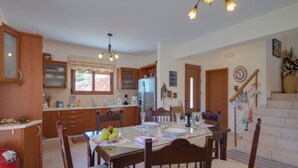 Una cocina amplia con armarios de madera, una mesa de comedor preparada para cuatro comensales y una escalera que sube a un nivel superior.