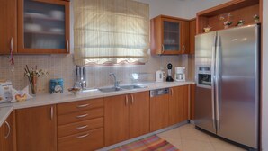 Una cocina con armarios de madera, un refrigerador de acero inoxidable, un lavamanos y una ventana con cortina.